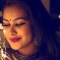 Portrait of a smiling woman adorned with lights and elegant jewelry, creating a warm, glamorous atmosphere.